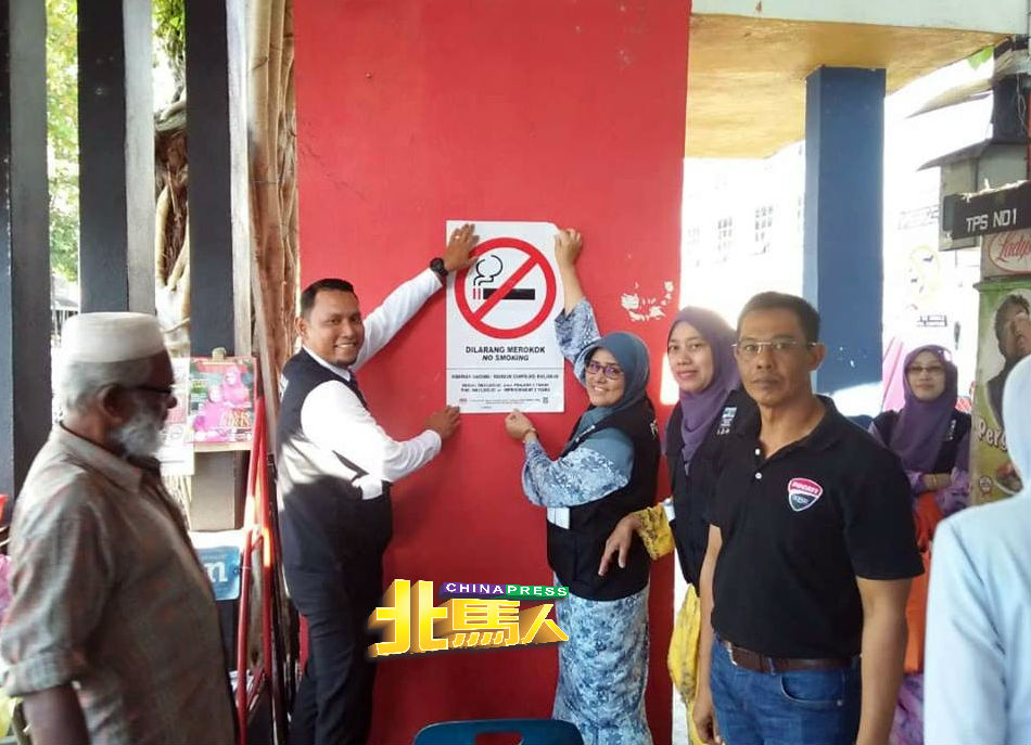罗基雅（左3）在小贩中心内，贴上40公分X50公分的禁烟告示。