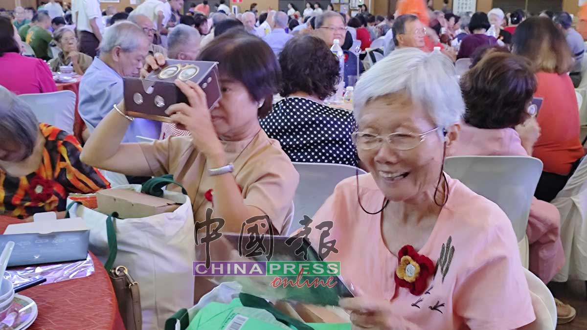 受惠的退休独中老师，在宴会上尝试使用虚拟现实眼镜（VR），来走进“师恩馆”重温昔日校园点滴。
